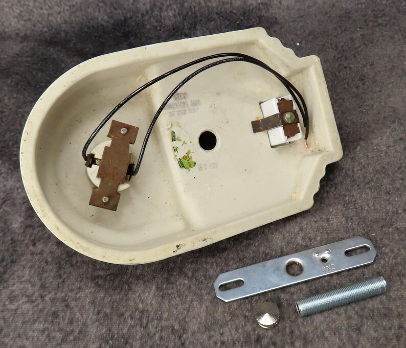 Puede incluir: Aplique de pared de cer&aacute;mica blanquecina con cableado negro y componentes met&aacute;licos. Incluye un soporte de montaje, una varilla roscada y una tapa decorativa. El aplique tiene forma ovalada curvada con borde decorativo.