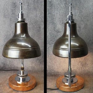 Puede incluir: Una l&aacute;mpara de escritorio de estilo vintage con una pantalla de color bronce y un v&aacute;stago y base cromados. La l&aacute;mpara tiene una base redonda de color cobre y un remate decorativo en la parte superior. La l&aacute;mpara est&aacute; enchufada.