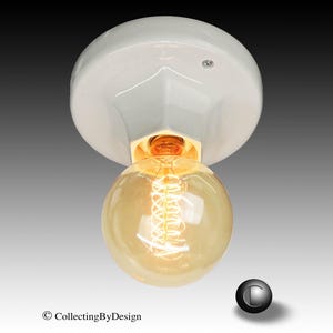 May include: A white porcelain ceiling light fixture with a glossy finish and a central socket. A round, amber-tinted glass light bulb with a visible glowing coiled filament is screwed into the base, emitting a warm light from the center.