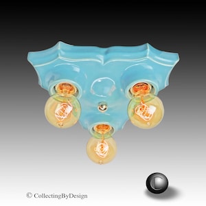 May include: A light blue ceramic flush mount ceiling light fixture with a scalloped edge design. The fixture features three circular sockets, each holding a round, amber-tinted Edison-style light bulb with a visible glowing filament inside.