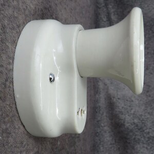 Puede incluir: Aplique de cer&aacute;mica blanquecina con base redondeada y casquillo acampanado en forma de trompeta. Un peque&ntilde;o tornillo plateado asegura la base. Dise&ntilde;ado para montaje en pared.