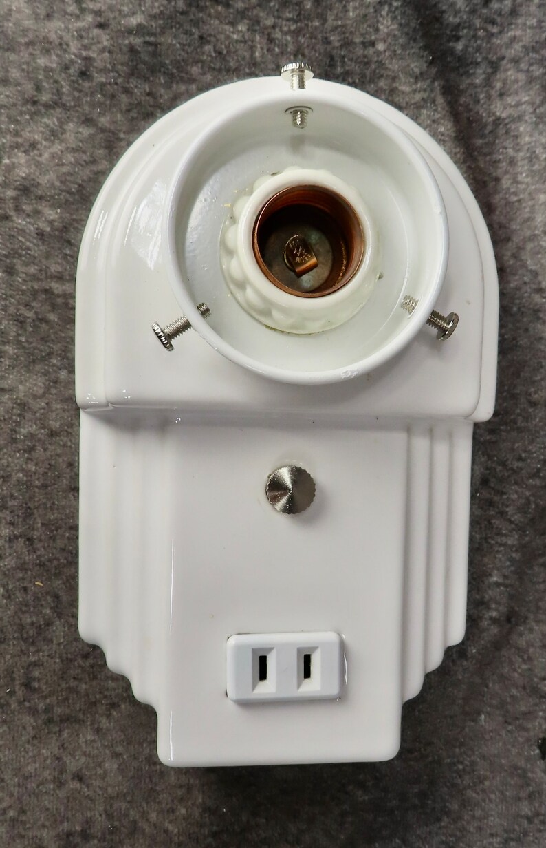 Puede incluir: Una l&aacute;mpara de cer&aacute;mica blanca con un portal&aacute;mparas, un enchufe y un dise&ntilde;o decorativo. La l&aacute;mpara tiene una parte superior redondeada y una base rectangular con un enchufe de dos clavijas.