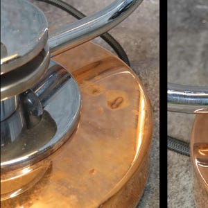 Puede incluir: Primer plano de una base de l&aacute;mpara vintage con una base circular de color cobre y un v&aacute;stago de metal cromado brillante. La base muestra signos de edad y desgaste, con un acabado ligeramente deslustrado. El dise&ntilde;o de la l&aacute;mpara es una mezcla de estilos industrial y retro.