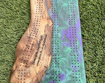 May include: A wooden and resin game board with a green and purple swirl design. The board has a quote inscribed on the wood side: "Some of the brightest lights come from the darkest places."