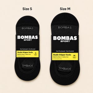 Pode incluir: Duas meias pretas Bombas Studio Gripper, tamanhos S e M, exibidas lado a lado. Cada meia &eacute; embalada com uma etiqueta preta e branca que diz "BOMBAS SPORT" e "Studio Gripper Socks". As meias s&atilde;o projetadas como meias de bal&eacute; sem mostrar.
