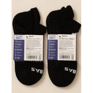 May include: Two black midweight socks with white dotted grips on the heel and sole. Each sock has a label with product details. The brand name "BAS" is printed in white on the bottom of each sock.