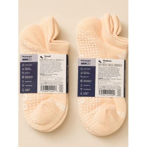 May include: Two pairs of peach-colored midweight socks with white grip dots on the soles. Each pair has a label with product information. One pair is size small, the other is medium.