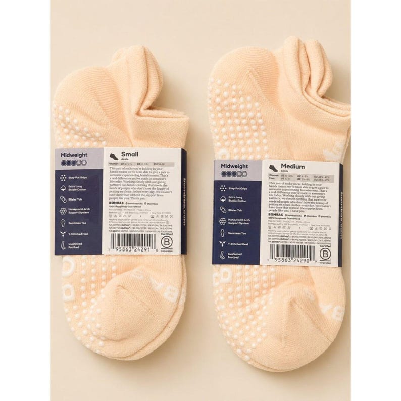 May include: Two pairs of peach-colored midweight socks with white grip dots on the soles. Each pair has a label with product information. One pair is size small, the other is medium.