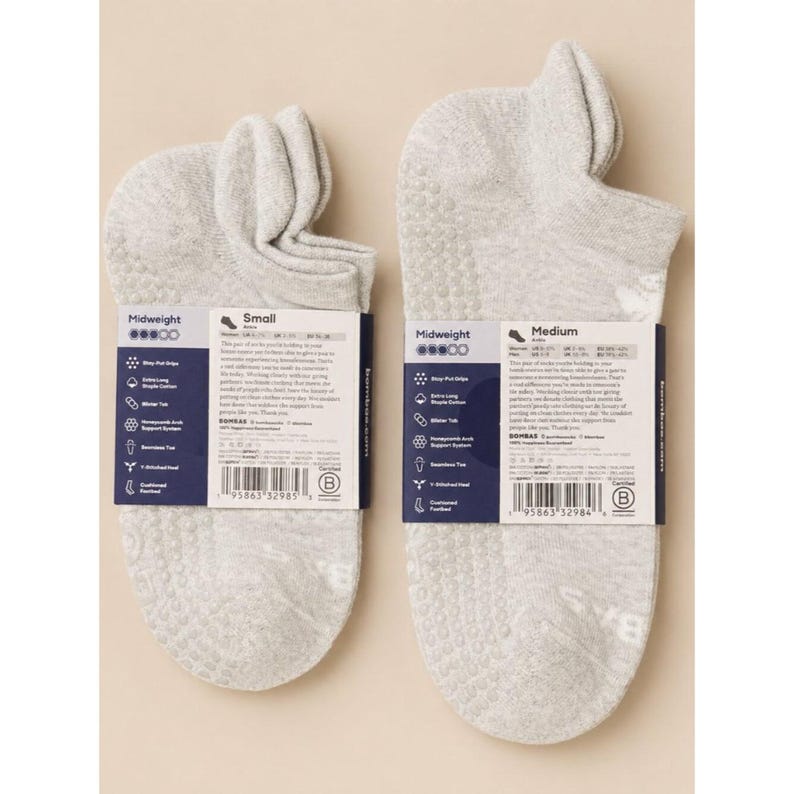 May include: Two pairs of light gray midweight socks with grip dots on the soles. Each sock has a label with product information. One label reads "Small" and the other reads "Medium".