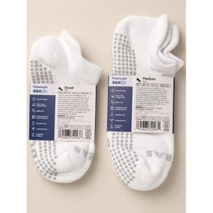 May include: Two pairs of white midweight socks with gray grip dots on the soles. One pair is labeled "Small" and the other "Medium". Each pair has a tag with product information and the brand name "BOMBAS".
