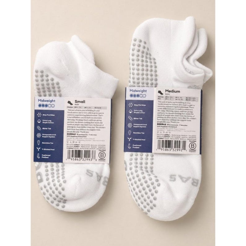 May include: Two pairs of white midweight socks with gray grip dots on the soles. One pair is labeled "Small" and the other "Medium". Each pair has a tag with product information and the brand name "BOMBAS".
