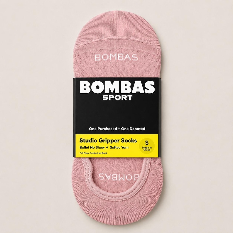 Pode incluir: Um par de meias Bombas Studio Gripper rosa claro, tamanho S, com a marca e "SPORT" em branco. A embalagem inclui o texto "One Purchased = One Donated" e "Ballet No Show".