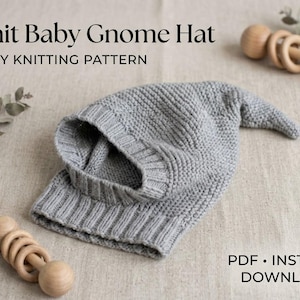 May include: A grey knit baby gnome hat with a ribbed brim and a pointed top. The text reads Knit Baby Gnome Hat EASY KNITTING PATTERN. There are wooden rattles and eucalyptus leaves nearby, with a PDF instant download icon in the corner.