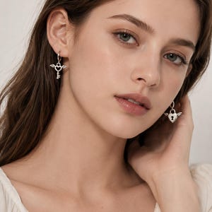 Puede incluir: Pendientes plateados con colgantes en forma de coraz&oacute;n y detalles de alas. Un pendiente presenta un dise&ntilde;o de llave, el otro un candado. Los pendientes tienen un estilo delicado y rom&aacute;ntico.