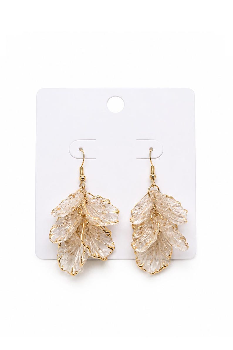 May include: A pair of dangle earrings with a leaf-like design. The earrings feature multiple layers of clear, textured, petal-shaped elements with gold-colored edges and hooks. They are displayed on a white card.