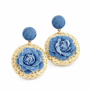 May include: A pair of dangle earrings featuring a circular woven straw base topped with a blue denim fabric flower. Each earring has a round blue denim stud post at the top, connected to the straw disc by a small gold-toned metal link.