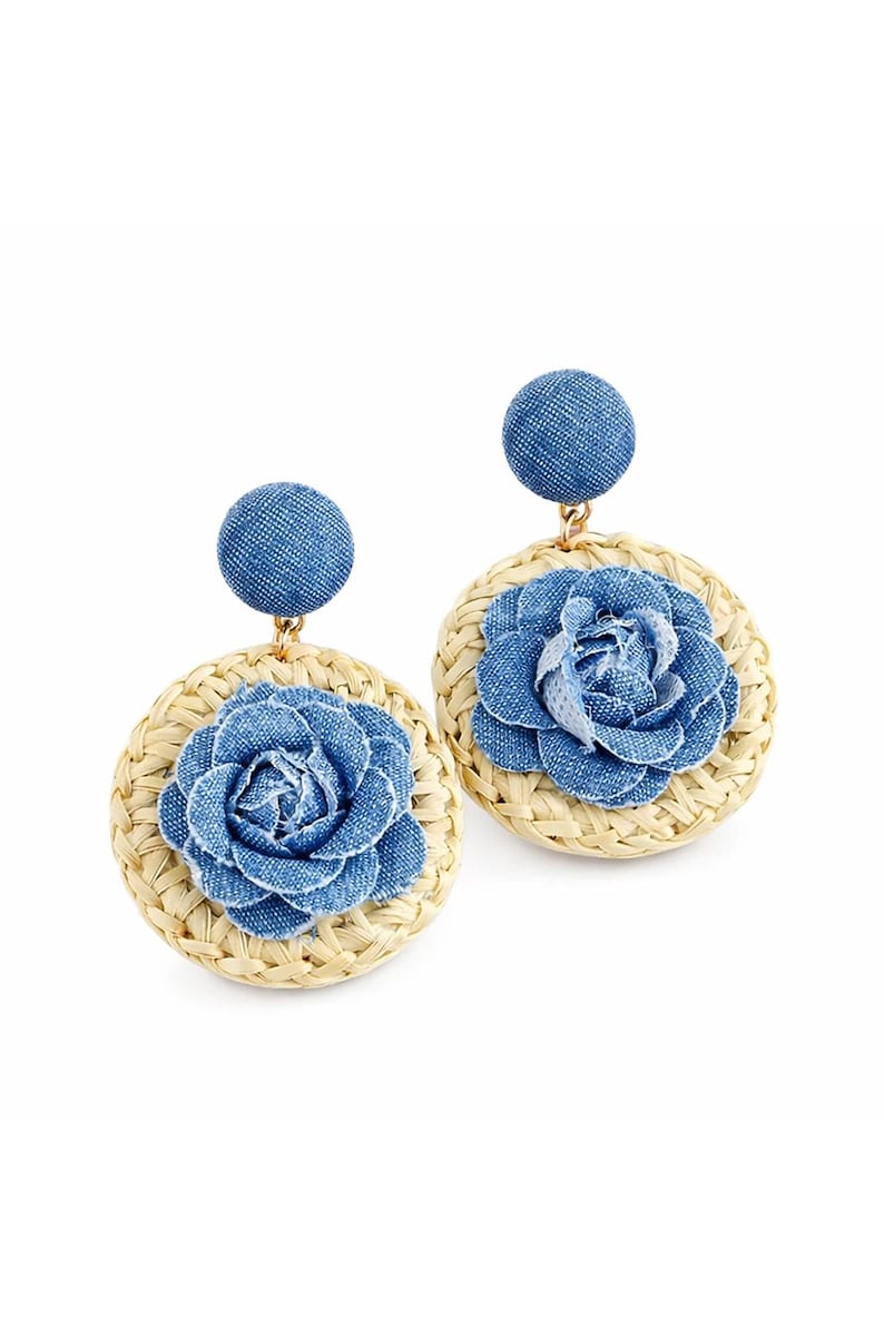 May include: A pair of dangle earrings featuring a circular woven straw base topped with a blue denim fabric flower. Each earring has a round blue denim stud post at the top, connected to the straw disc by a small gold-toned metal link.