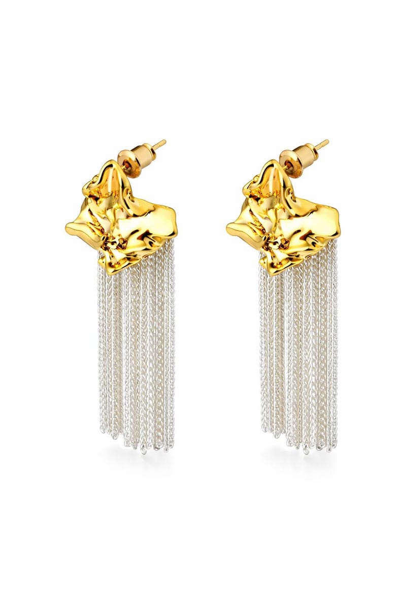 May include: A pair of gold-tone earrings with a textured, organic shape at the top and cascading silver-tone chain fringe. The earrings have a post-back closure and are displayed against a white background.