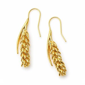 May include: A pair of gold-colored earrings. Each earring features a stylized wheat stalk design, with a curved hook for the ear. The earrings are set against a white background, highlighting their intricate details and golden hue.