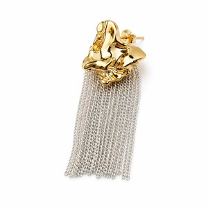 May include: A single gold-colored earring with a textured, organic shape. The earring features a cascade of silver-colored chain fringe, creating a striking contrast. The earring is designed to be worn in a pierced ear.