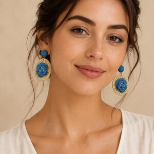 May include: Dangle earrings featuring a circular woven straw base in a natural beige tone, centered with a blue fabric rose. The top of each earring consists of a small, round, blue fabric-covered stud, connecting to the larger circular pendant.