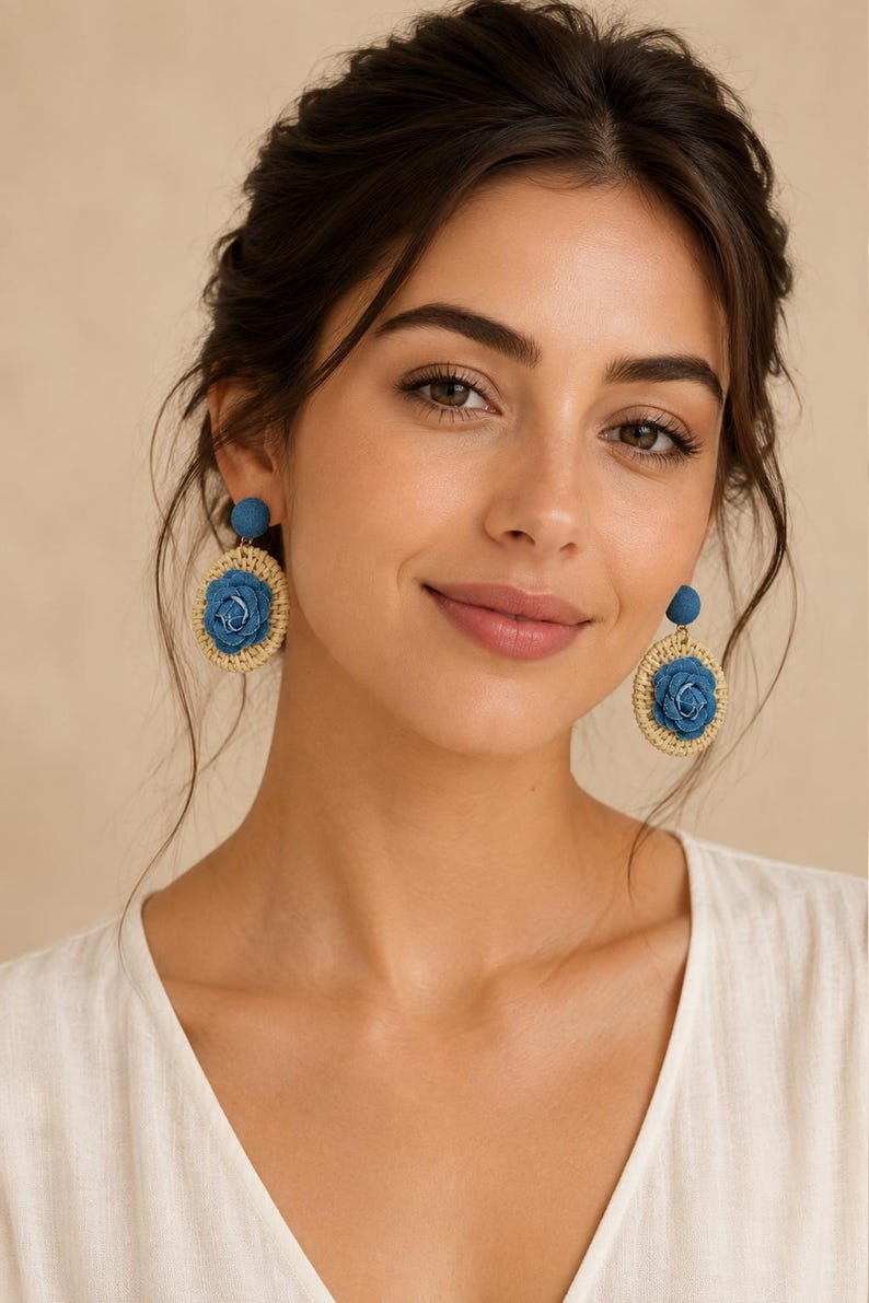 May include: Dangle earrings featuring a circular woven straw base in a natural beige tone, centered with a blue fabric rose. The top of each earring consists of a small, round, blue fabric-covered stud, connecting to the larger circular pendant.