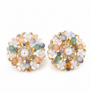 May include: A pair of gold-coloured, floral-shaped earrings. Each earring features a central pearl surrounded by small, colourful beads in shades of peach, green, and grey. The outer edge is adorned with white flower-shaped accents.