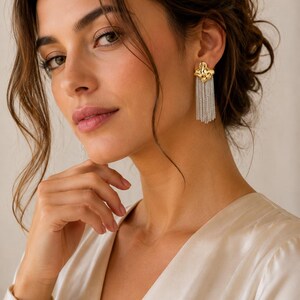 May include: Gold-tone and silver-tone chain tassel earrings. The earrings have a textured gold-tone top with dangling silver-tone chains. The model is wearing a cream-colored satin top.