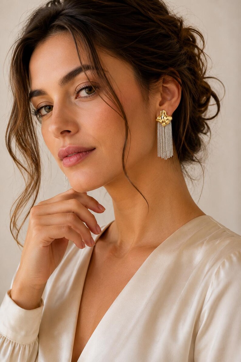 May include: Gold-tone and silver-tone chain tassel earrings. The earrings have a textured gold-tone top with dangling silver-tone chains. The model is wearing a cream-colored satin top.