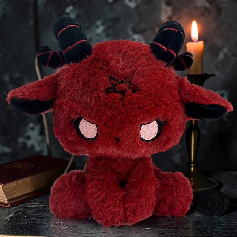 May include: A plush red goat with black horns and ears, and a pentagram on its forehead. The stuffed animal has pink eyes and is sitting down. The plush toy is a unique gothic-themed item.