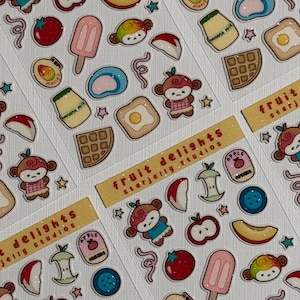 May include: A sticker sheet titled fruit delights starjelly studios featuring various illustrations including monkeys, apple slices, apple cores, red tomatoes, pink popsicles, blue mochi, banana milk cartons, waffles, fried eggs, and small stars.