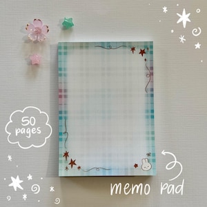 May include: A rectangular memo pad featuring a light blue and white plaid border. The paper includes decorative brown star icons, swirling line accents, and a small white rabbit illustration in the bottom right corner. The text 50 pages is visible.