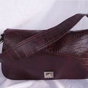 May include: A dark brown leather shoulder bag with a crocodile-embossed pattern. The bag has a flap closure with a silver buckle.