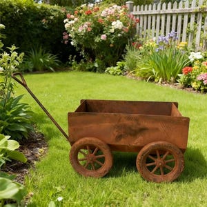 May include: A weathered, rusty brown metal garden cart with two spoked wheels and a long handle. The cart sits on a green lawn, with a garden and white picket fence in the background. The cart is designed for outdoor use.