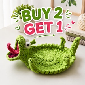 Könnte beinhalten: Ein leuchtend grünes Häkeltablett in Form eines Cartoon-Alligators mit offenem Maul, das eine rosa Zunge und ein dunkles Inneres zeigt. Der Text BUY 2 GET 1 ist in großen grünen und rosa Buchstaben über der handgefertigten Garnfigur zu sehen.