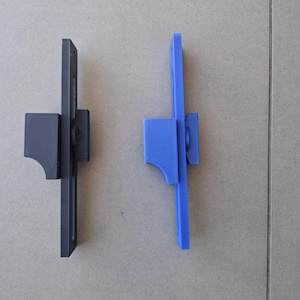 May include: Two 3D-printed brackets are shown, one dark grey and one bright blue. Each has a rectangular vertical section and a horizontal section with a curved edge. The design suggests they are for mounting or support, against a neutral backdrop.