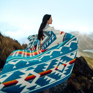 May include: A turquoise, white, and red patterned blanket with geometric designs. The blanket has a vibrant color palette and is draped over a person. The blanket's design includes triangles, diamonds, and stripes, creating a Southwestern or Native American aesthetic.