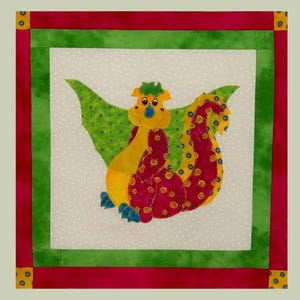 May include: A colorful, whimsical quilt square featuring a cartoon dragon. The dragon has yellow, red, and blue accents, with green wings. The square is bordered by red, green, and yellow fabric, creating a vibrant, playful design.