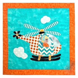 May include: A colorful, handmade fabric art piece featuring a helicopter design. The helicopter has a polka-dot body, a chevron pattern, and a smiling pilot. The background is turquoise with white clouds, framed by an orange border.