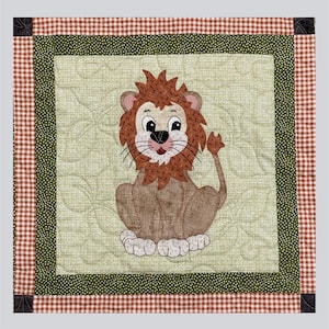 May include: A square quilted wall hanging featuring a central light green panel with a stitched lion appliqué. The lion has a brown mane, tan body, and white paws. The border consists of a dark green dotted fabric and an outer orange gingham frame.