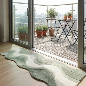 May include: A long, rectangular runner rug featuring a wavy, organic pattern in shades of sage green and cream. The rug has a textured, tufted surface with curved edges that follow the undulating design, creating a soft, flowing visual effect.