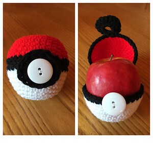 May include: A red, white, and black crocheted Pokeball with a white button. The Pokeball is open and an apple is inside.