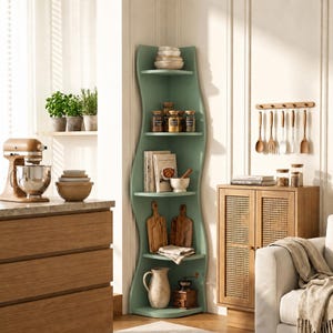 May include: A sage green corner shelving unit with five curved shelves. The shelves hold stacked bowls, glass jars with spices, books, two wooden cutting boards, a white ceramic pitcher, a small white bowl, and a wooden coffee grinder.