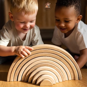 Puede incluir: Un juguete apilable de madera en color natural claro con forma de arcoíris, compuesto por diez arcos semicirculares encajables. Los arcos están dispuestos en formación curva, disminuyendo de tamaño desde el exterior hacia el centro.