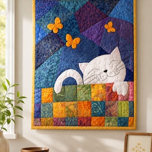 May include: A rectangular fabric wall hanging featuring a white cat with closed eyes peeking over a multicolored patchwork quilt. The background consists of blue and purple geometric fabric pieces with three bright orange butterflies attached.