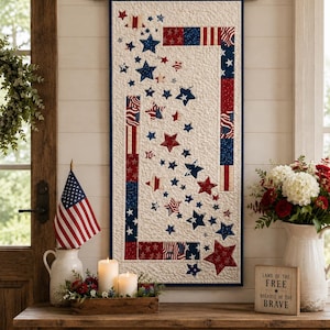 May include: A rectangular wall hanging quilt featuring a cream-colored background with a cascading pattern of red, white, and blue stars. The quilt is framed by vertical and horizontal fabric strips in patriotic patterns and hangs from a wooden rod.
