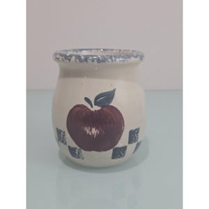 Puede incluir: Un tarro de cerámica de color crema con cuerpo redondeado y boca ancha. El exterior presenta una manzana de color rojo oscuro pintada a mano con una hoja verde en el centro, rodeada por un patrón de pequeños cuadrados azul oscuro en la base.