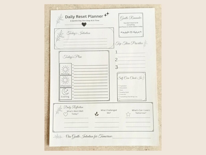 May include: A white Daily Reset Planner sheet with black text and line art. Sections include Today's Intention, Top Three Priorities, Today's Plan with morning, afternoon, and evening icons, a Self-Care Check-In, Daily Reflection, and One Gentle Intention for Tomorrow.