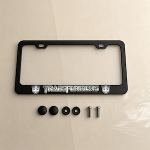 May include: Black license plate frame with the word "TRANSFORMERS" in silver lettering. The frame includes the Transformers logo on each side. Also included are black screw caps and screws.