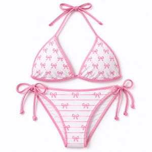 May include: A white bikini set with a pink bow pattern. The top is a halter neck style, and the bottoms have tie sides. The edges are trimmed in pink. The set is designed for swimwear.